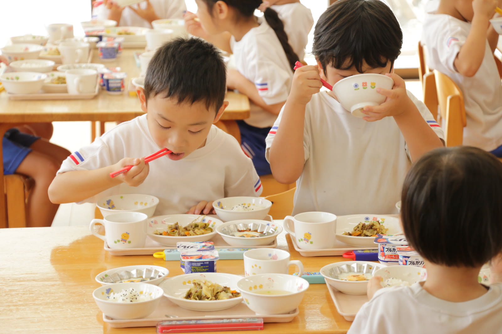 お箸やお椀を使って給食を食べる子どもたち